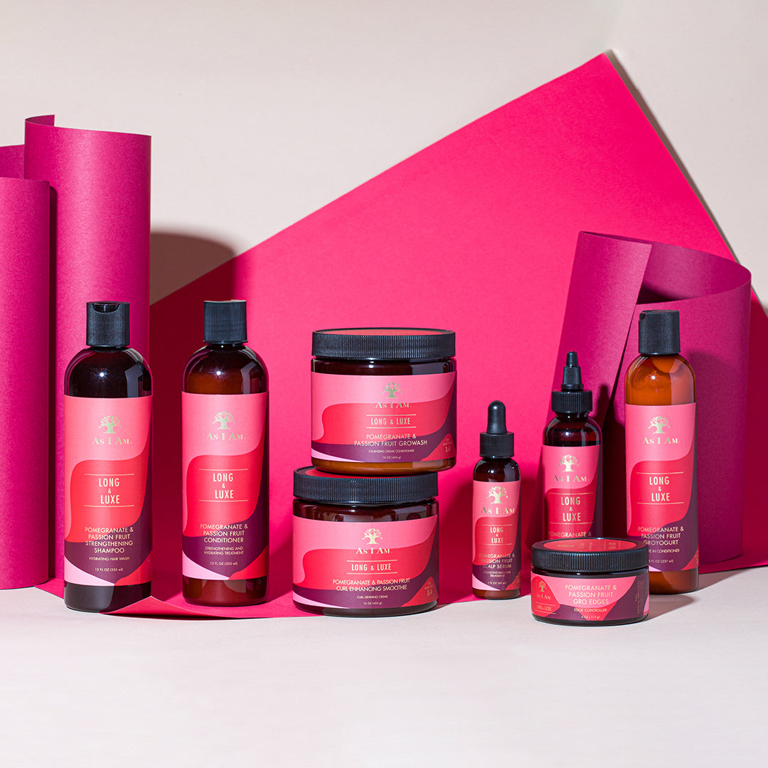 Billedet viser As I Am Long and Luxe Strengthening Shampoo, Conditioner, GroHair Oil og andre produkter fra serien. Produkterne er arrangeret foran en pink baggrund.