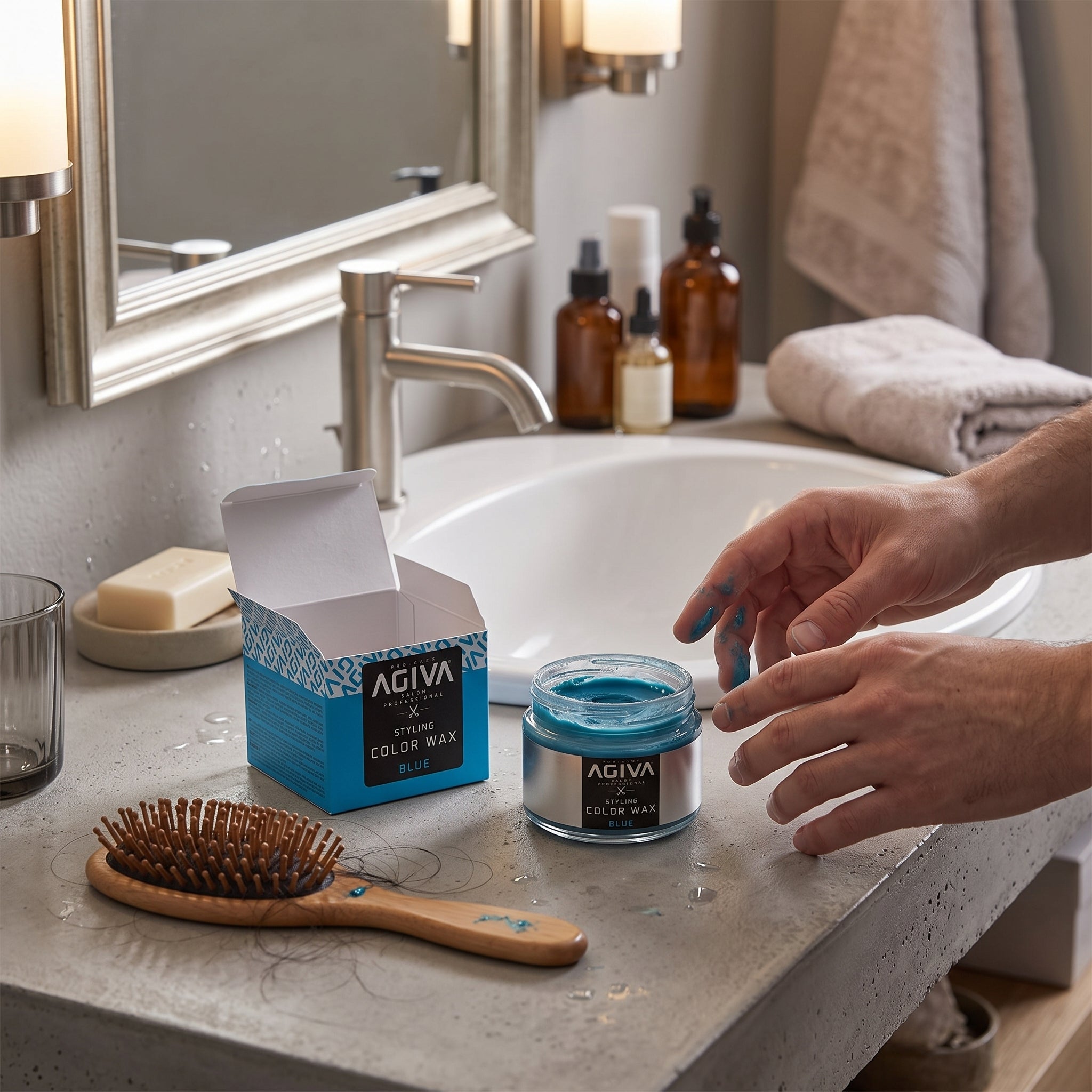 Agiva Styling Color Wax Blue i åben glaskrukke på badeværelsesbord med hænder farvet blå og hårbørste.