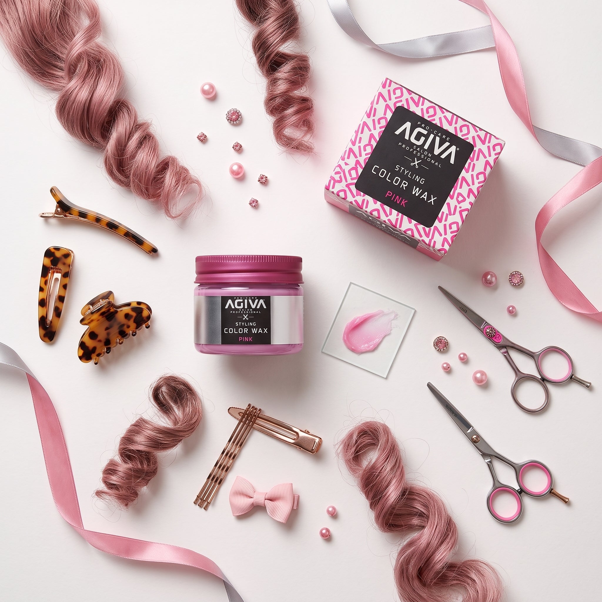 AGIVA Styling Color Wax Pink krukke omgivet af rosa krøllet hår, hårspænder, sløjfe, saks og perler.