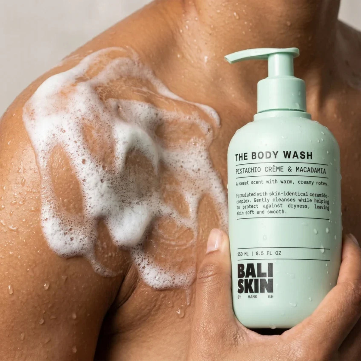 Bali Skin The Body Wash pumpeflaske i mintgrøn holdes op mod skulder dækket af hvidt sæbeskum.
