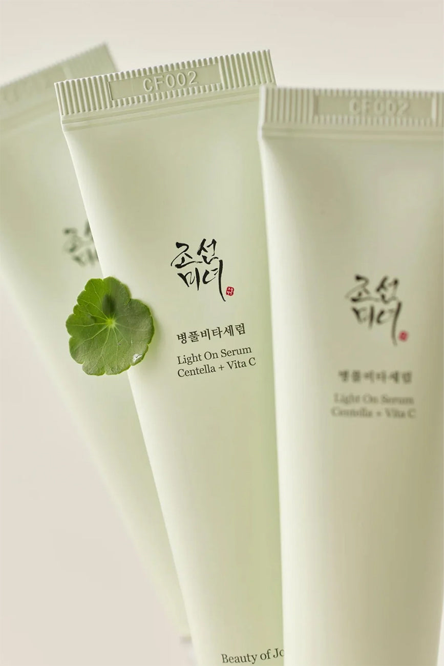 Flere tuber af Beauty of Joseon Light On Serum Centella + Vita C 30ml med centella-blad i fokus på beige baggrund.