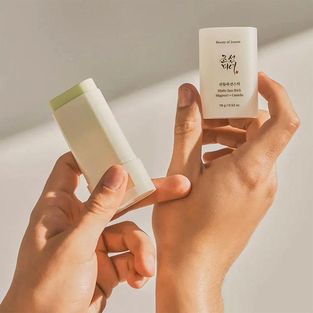 To hænder holder Beauty of Joseon Matte Sun Stick Mugwort + Camelia 18gr i sollys med synlig grøn stift og elegant emballage.