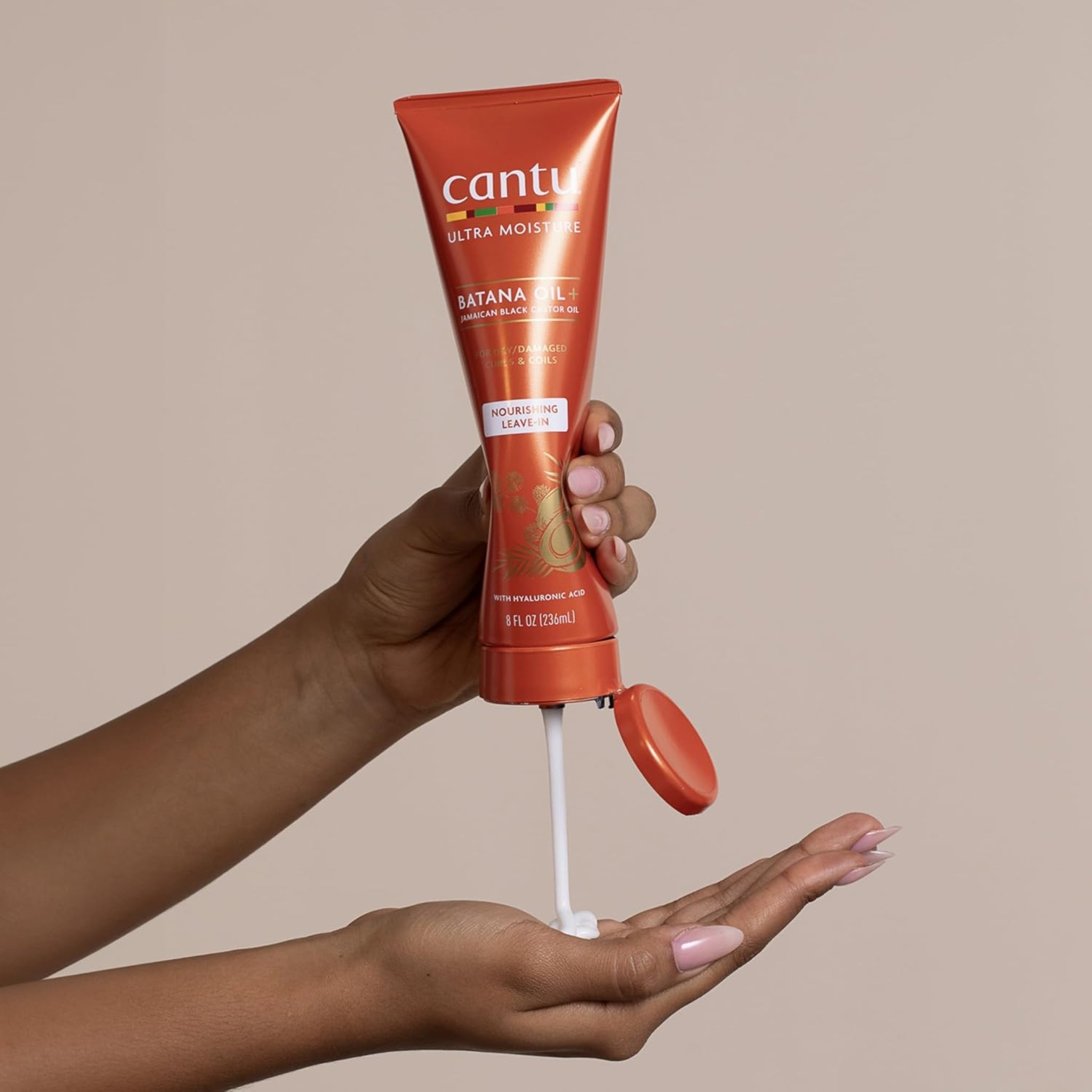 Hånd klemmer Cantu Ultra Moisture Batana Oil+ nourishing leave-in creme ud i håndfladen på en anden hånd.