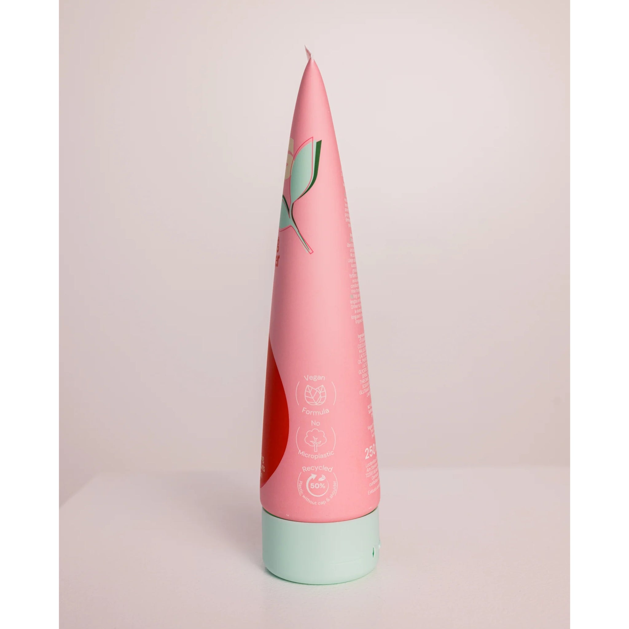 Lyserød tube hårshampoo med mintgrøn låg, mærket med veganske og genbrugsvenlige ikoner.