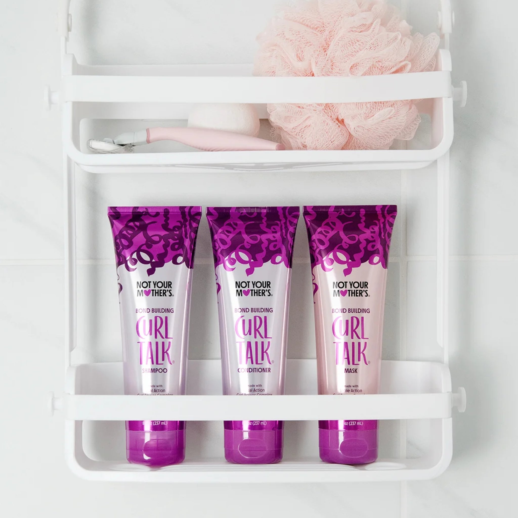 Not Your Mother's Curl Talk shampoo, conditioner og maske i lilla tuber på hvid badehylde med pink svamp.