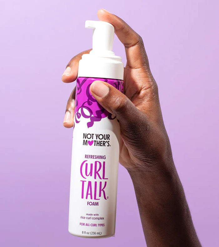 Hånd holder Not Your Mother's Curl Talk Refreshing Foam 236ml mod lilla baggrund – ideel til alle krølletyper.