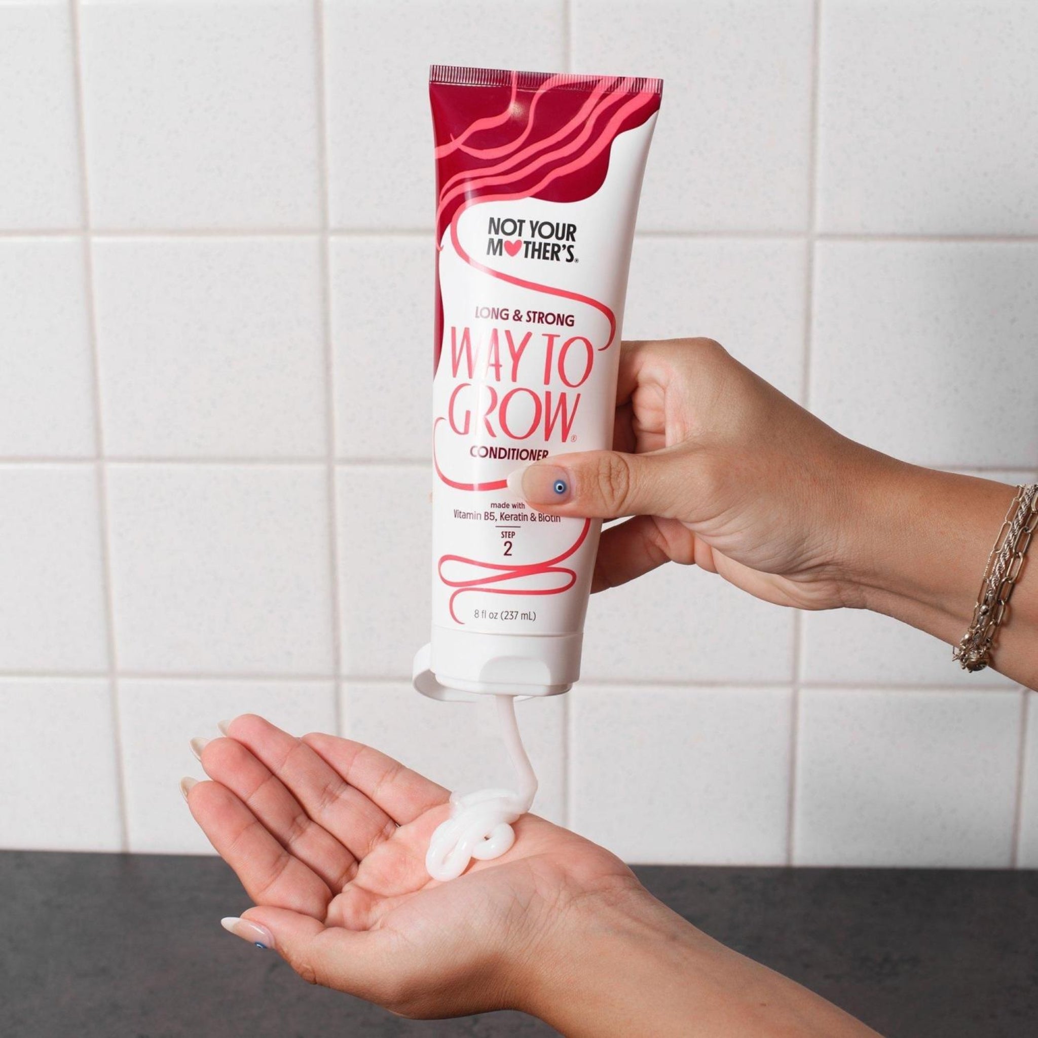 Not Your Mother's Way To Grow Conditioner trykkes ud i hånd foran hvide fliser.