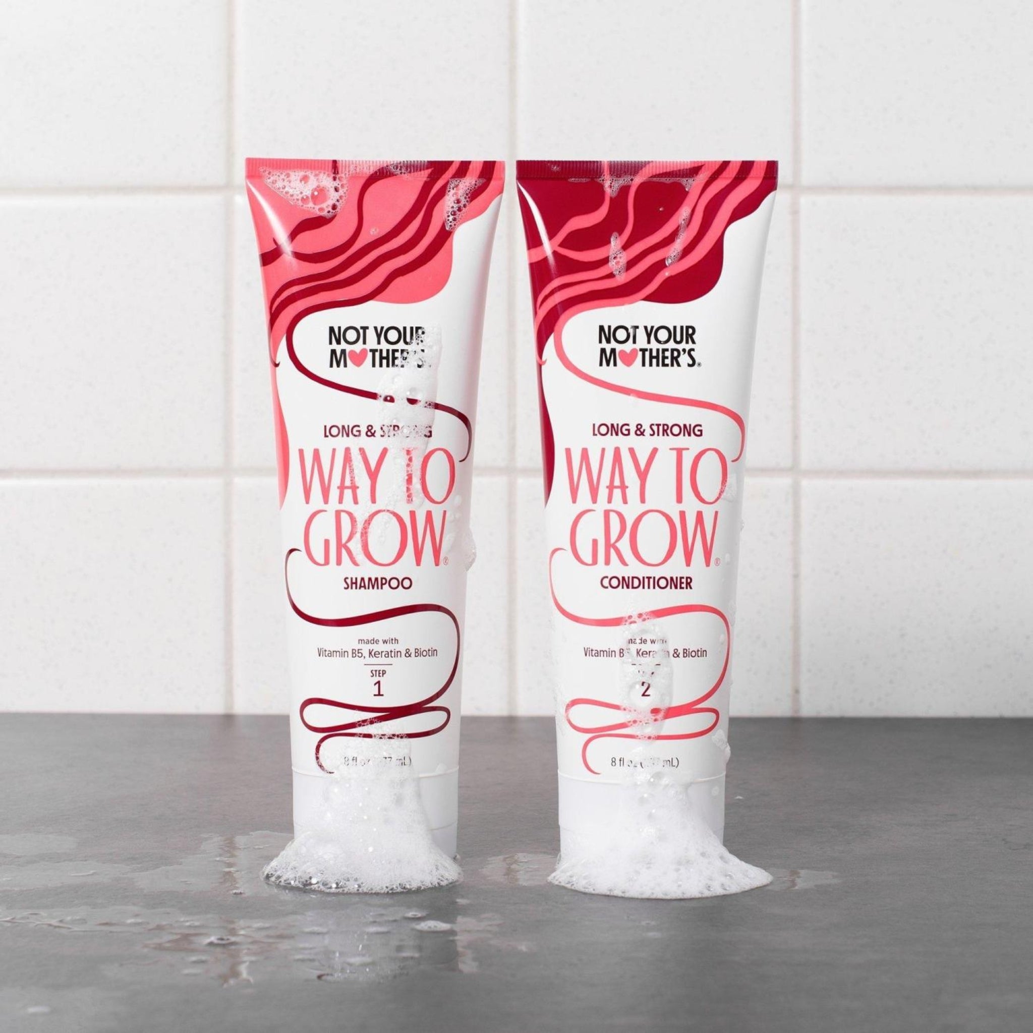 Not Your Mother's Way To Grow shampoo og conditioner i pink-hvide tuber med skum på grå overflade.