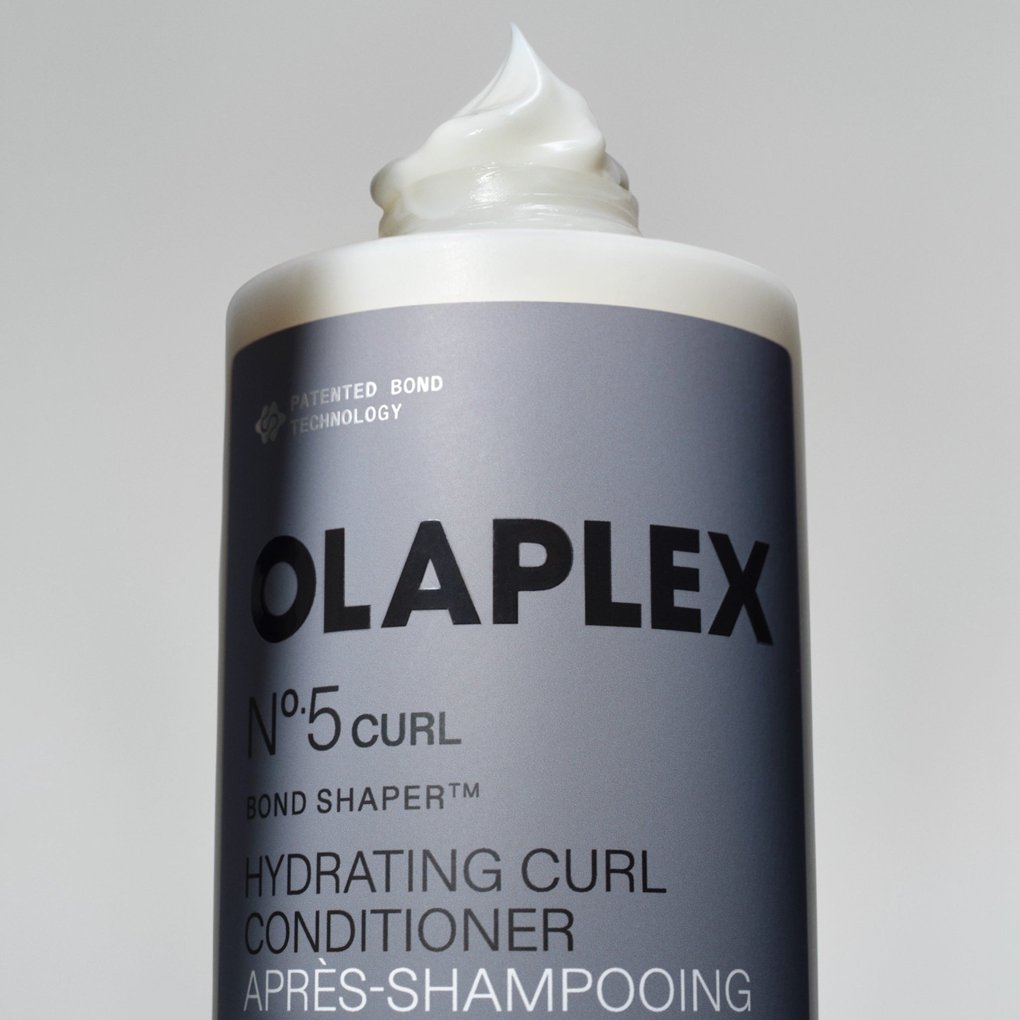 Olaplex Nº.5 Curl Bond Shaper hydrerende curl conditioner i grå flaske med cremet produkt på toppen.