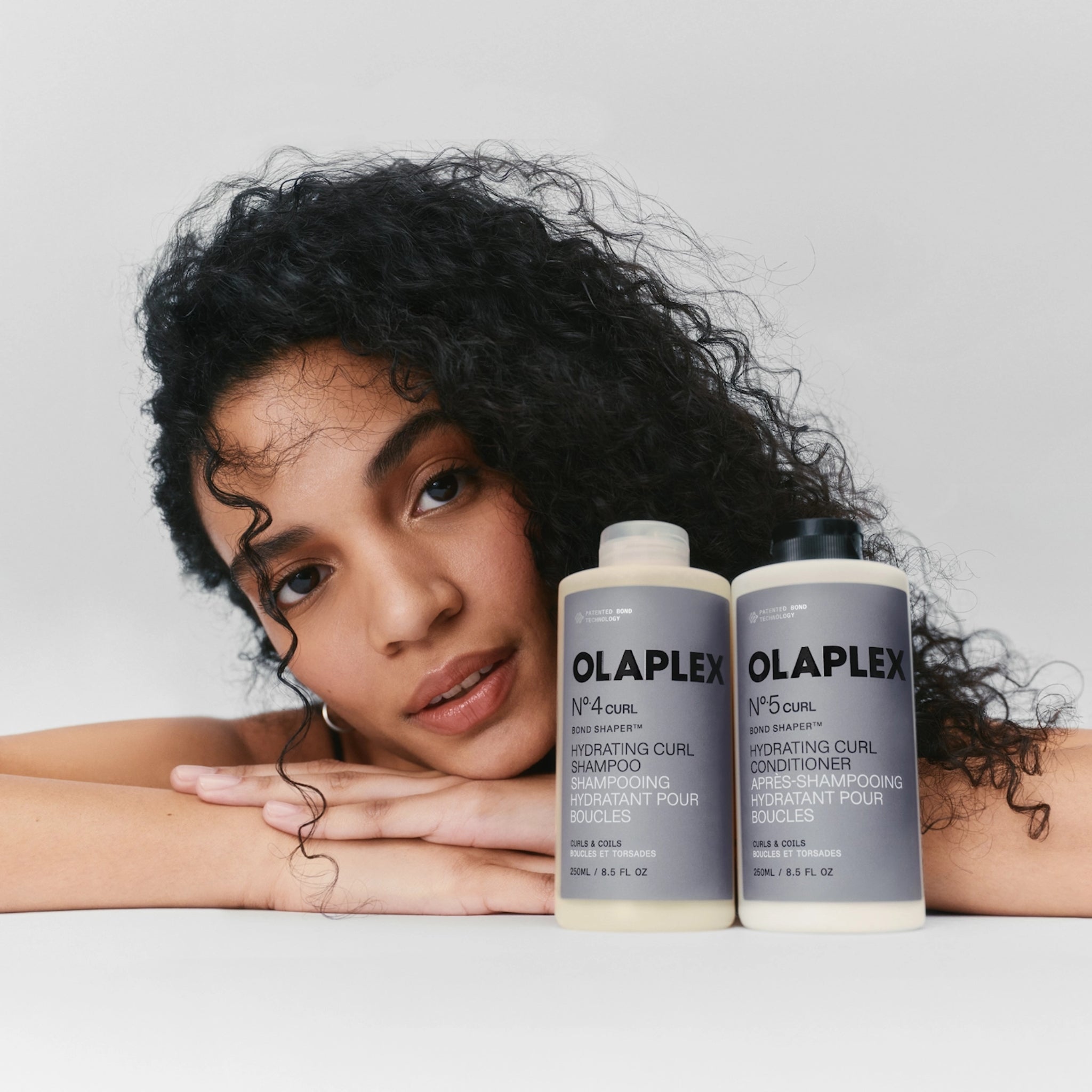 Kvinde med krøllet hår ved siden af Olaplex No.4 og No.5 Curl hydrerende shampoo og balsam til krøller.